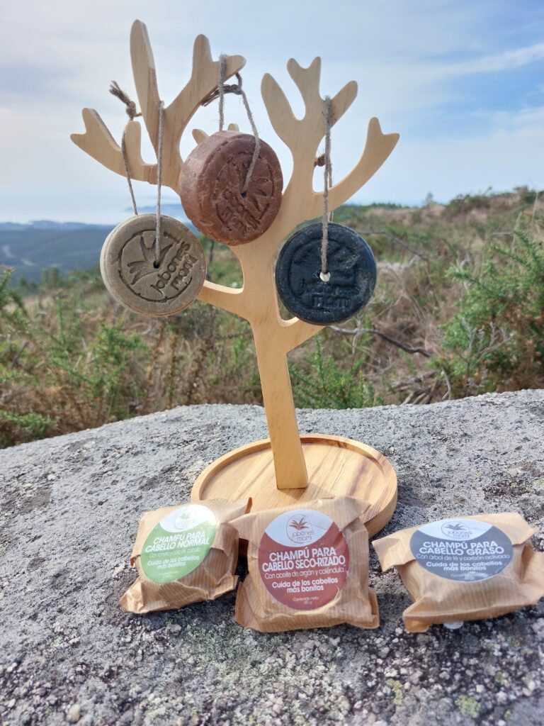 Champús sólidos de Jabones Mami colgados de su cordón en un árbol de madera, con sus envases de papel