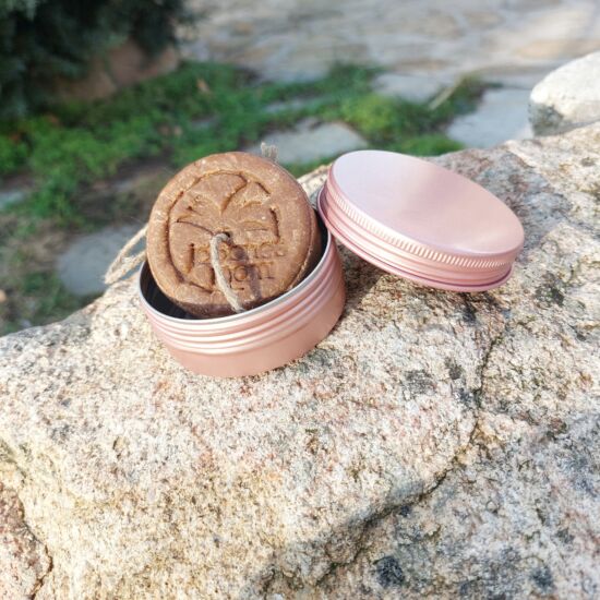 Champú sólido para cabello seco con su lata de viaje rosa, sobre piedra