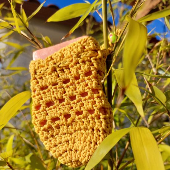 Porta jabones de ganchillo color mostaza, hecho a mano, entre plantas